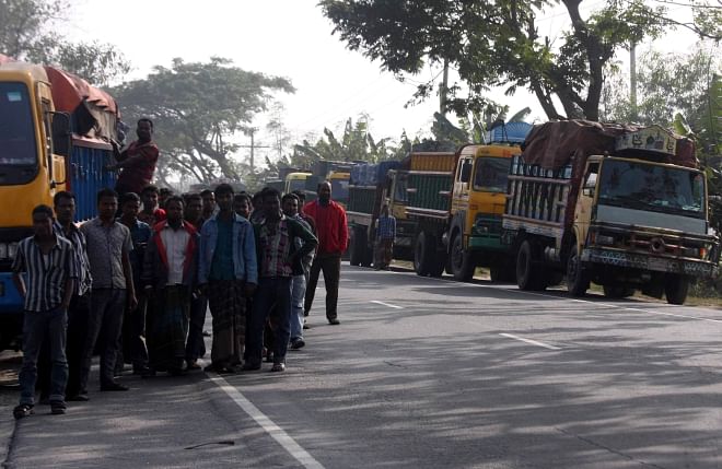 Drivers of goods laden trucks anxiously 'wait for their turn' near their vehicles a little away from the 'extortionist' law enforcers at Gharinda Bypass point on Dhaka-Tangail Highway on Tuesday afternoon. PHOTO: STAR