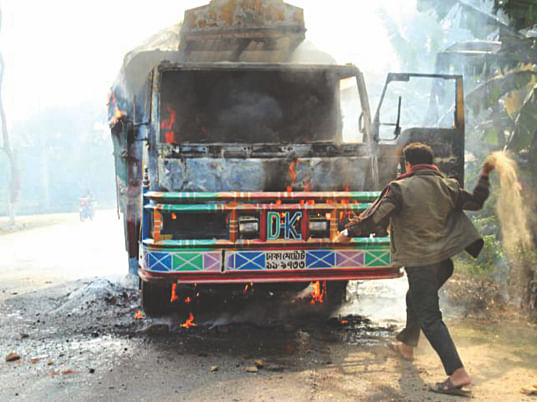 Robbed Of Livelihood: In desperation, Ratan Mia throws a fist full of sand into the burning truck at Jhopgari in Bogra yesterday. He along with law enforcers and locals, who arrived at the scene later on, made several attempts to save the vehicle Ratan himself owns. It was what put food on his table. Unable to save it. Photo: star