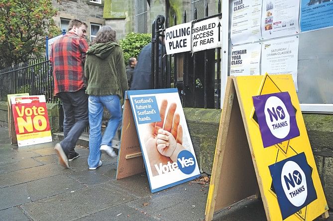 Voters walks past campaign posters outside a polling station in Edinburgh yesterday, during Scotland's independence referendum.  Photo: AFP