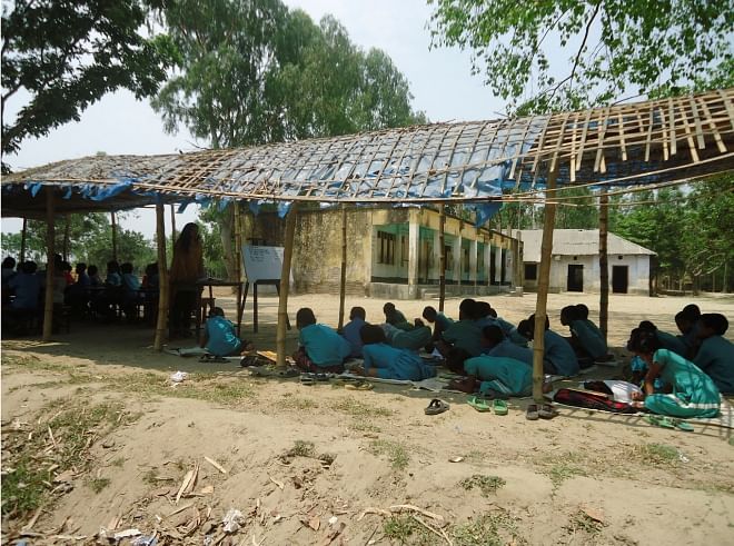 Students of Rajagaon Government Primary school at Rajagaon village in Thakurgaon Sadar upazila attend classes under a makeshift shed as the school building was declared abandoned in June last year after cracks developed on its walls and floors. Photo: Star