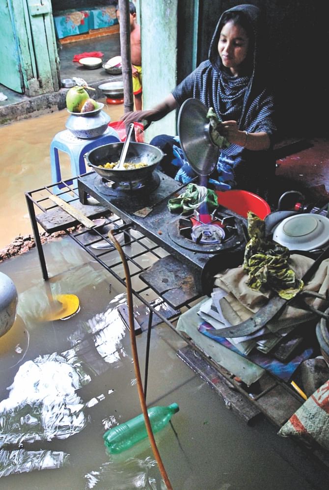 A woman cooks in her kitchen, that had been flooded. Photo: Anisur Rahman