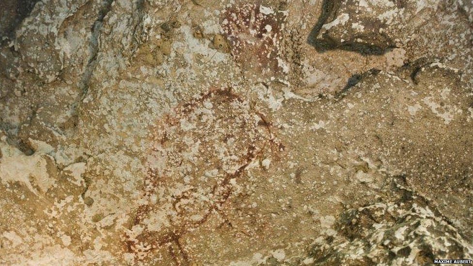 At the top of the worn painting is a faint outline of a human hand. Below it is possibly the earliest depiction of an animal. Photo taken from BBC