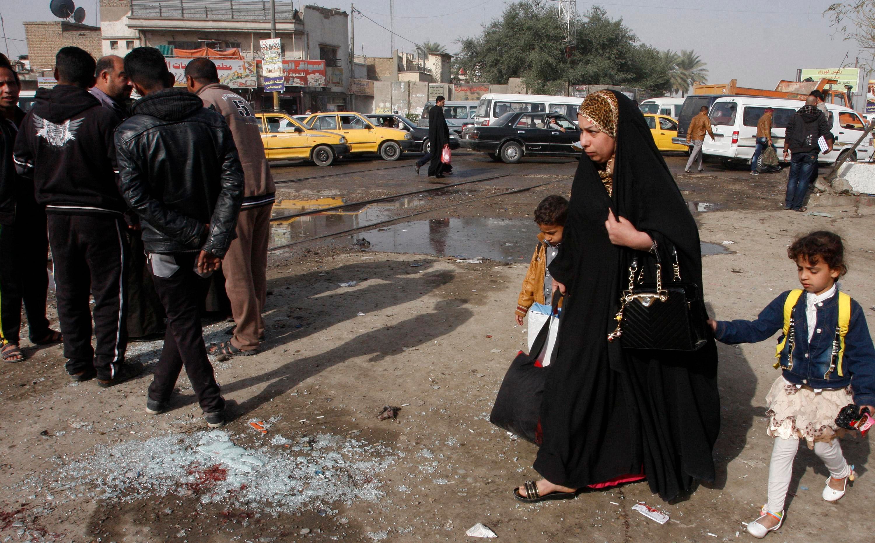 A woman with her children walks past at the site of a suicide bombing attack in the Shi'ite neighborhood of Kadhimiya in Baghdad February 9, 2015. Photo: Reuters