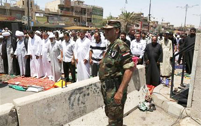 A member of the Iraqi security forces stands next to followers of Shiite cleric Muqtada al-Sadr attending open-air Friday prayers in the Shiite stronghold of Sadr City, Baghdad, Iraq, Friday, July 18, 2014. Photo: AP