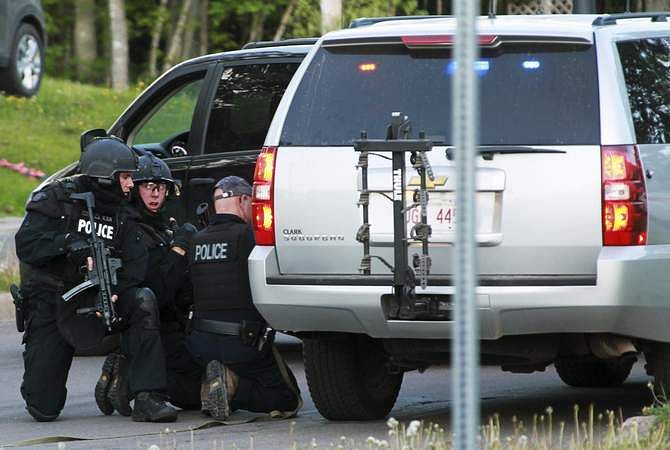 Emergency Response team members take cover behind vehicles in Moncton, New Brunswick June 4, 2014. Three police officers were shot dead and two more were wounded, police said as they conducted a manhunt for a man carrying a rifle and wearing camouflage clothes. Photo: Reuters