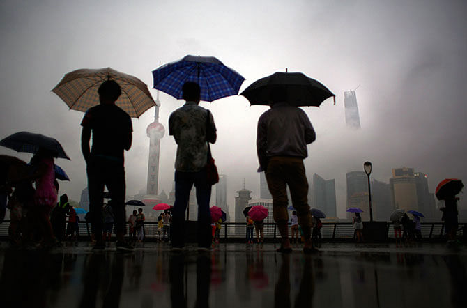 People stand under heavy rain at the Bund in front of the financial district of Pudong, in downtown Shanghai August 18, 2014. Photo: Reuters