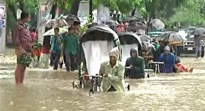 People try to get to work on rickshaw ploughing through over knee-deep water on a street in an area of Chittagong city Saturday as overnight heavy showers that stopped in the morning inundate several areas of the port city. Photo: TV grab