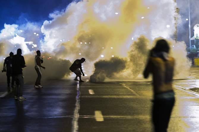A protester reaches down to throw back a smoke canister as police clear a street after the passing of a midnight curfew meant to stem ongoing demonstrations in reaction to the shooting of Michael Brown in Ferguson, Missouri August 17, 2014. Photo: Reuters