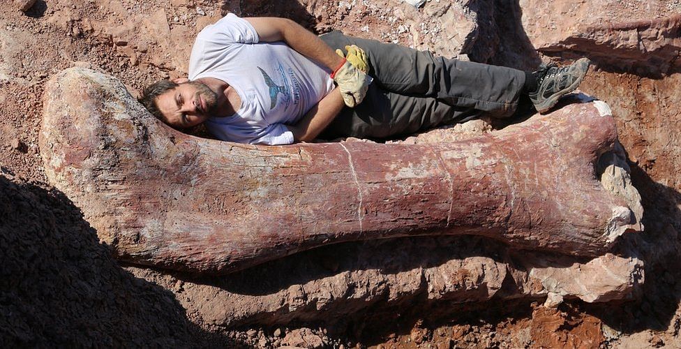 Dr Diego Pol lies on a dinosaur bone. Photo: BBC