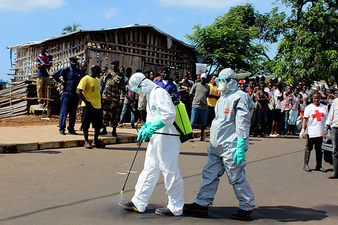 Health workers spray themselves with chlorine disinfectants after removing the body a woman who died of Ebola virus in the Aberdeen district of Freetown, Sierra Leone, October 14, 2014. Photo: Reuters
