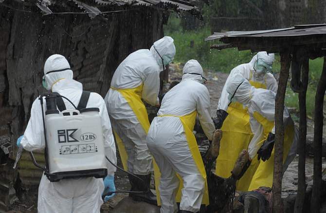 Health workers wearing protective clothing carry an abandoned dead body presenting with Ebola symptoms at Duwala market in Monrovia August 17, 2014. To try to control the Ebola epidemic spreading through West Africa, Liberia has quarantined remote villages at the epicentre of the virus, evoking the 
