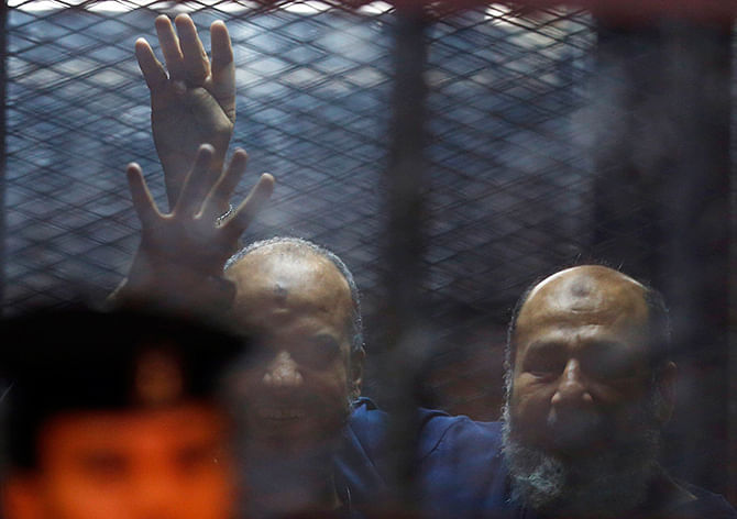 Muslim Brotherhood's senior member Mohamed El-Beltagy and Islamist cleric Safwat Hegazis (R) gestures the four-fingered "Rabaa" hand symbol behind bars and glass panels from the defendant's cage at a courtroom in Cairo August 7, 2014. Photo: Reuters