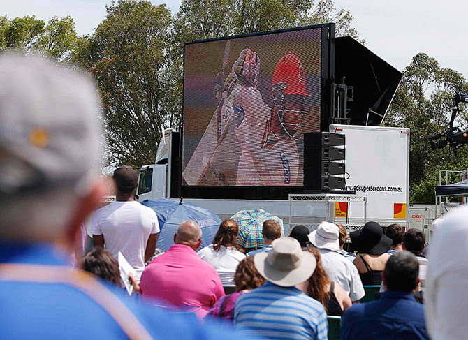 Locals observe a picture of Australian cricketer Phillip Hughes from a sports field during a live telecast of his funeral nearby in his home town of Macksville, December 3, 2014. Photo: Reuters