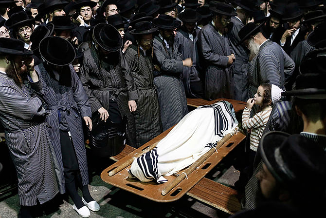 The young son of Abraham Wallace stands next to his covered body along with other ultra-Orthodox Jews at Wallace's funeral in Jerusalem's Mea Shearim neighbourhood August 4, 2014. Photo: Reuters