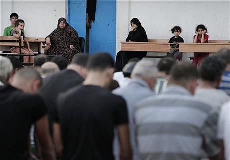 Palestinians displaced people watch as men pray in the courtyard of a U.N. school in Gaza City, Monday. Photo: AP