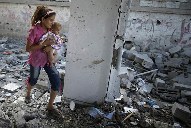A Palestinian girl holding her sister walks through debris near remains of a mosque, which witnesses said was hit by an Israeli air strike, in Beit Hanoun in the northern Gaza Strip August 25, 2014. Photo: Reuters