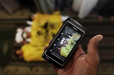 A man takes a photo with his mobile phone of the lifeless bodies of Qasim Alwan, 4, Imad Alwan, 6, and Rizk Hayek, 1, who were killed Friday by an Israeli tank shell, during their funeral in Gaza City, Saturday, July 19. Photo: AP