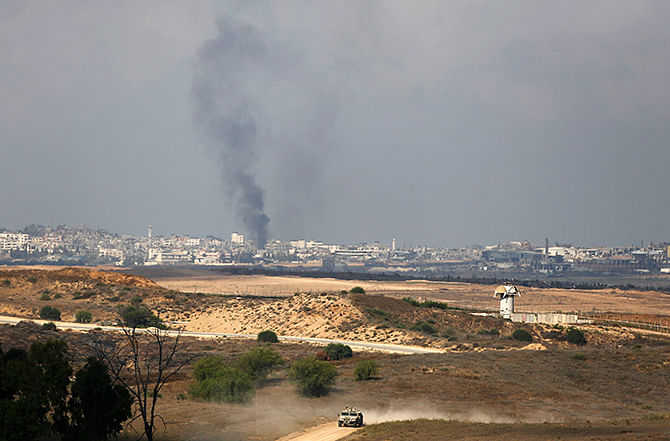 Rising smoke after an Israeli strike can be seen in the Gaza Strip as an Israeli military vehicle drives on the Israeli side of the border August 8, 2014. The Israeli military responded with air strikes at 