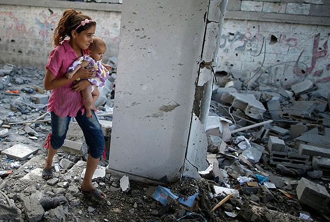 A Palestinian girl holding her sister walks through debris near remains of a mosque, which witnesses said was hit by an Israeli air strike, in Beit Hanoun in the northern Gaza Strip August 25. Photo: Reuters