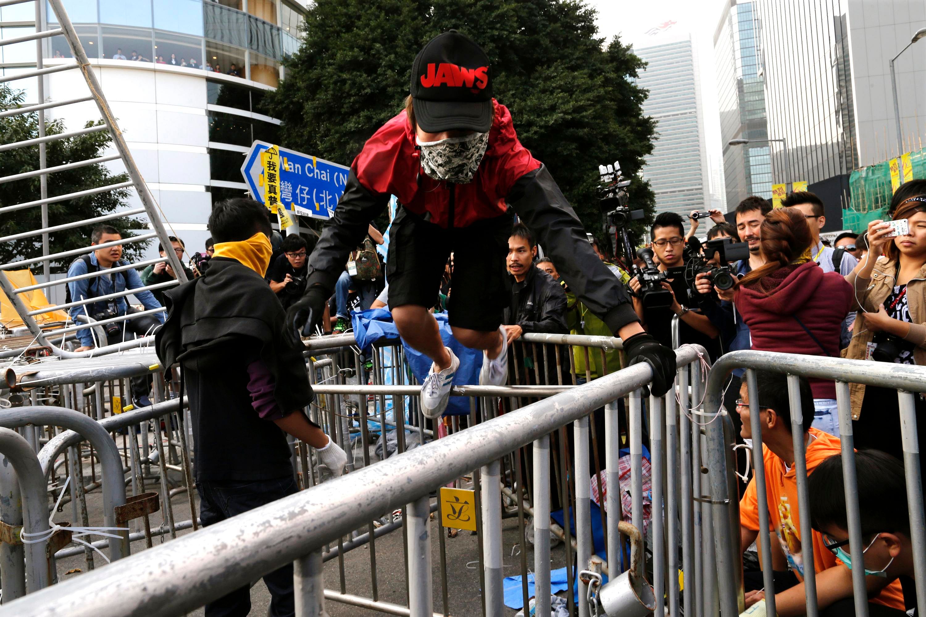 A masked pro-democracy protester climbs on a barricade after the arrival of bailiffs under a court injunction to clear up part of the protest site, outside the government headquarters in Hong Kong November 18. Photo: Reuters 