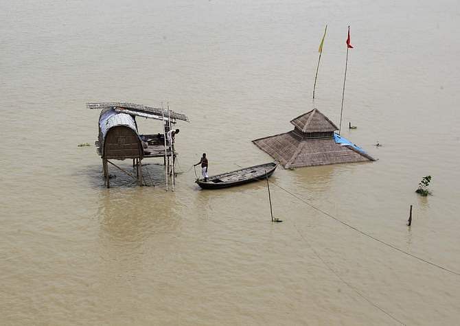 A sadhu or Hindu holy man stands on a boat near a submerged hut on the flooded banks of river Ganga after heavy monsoon rains in the northern Indian city of Allahabad August 9, 2014. Photo: Reuters