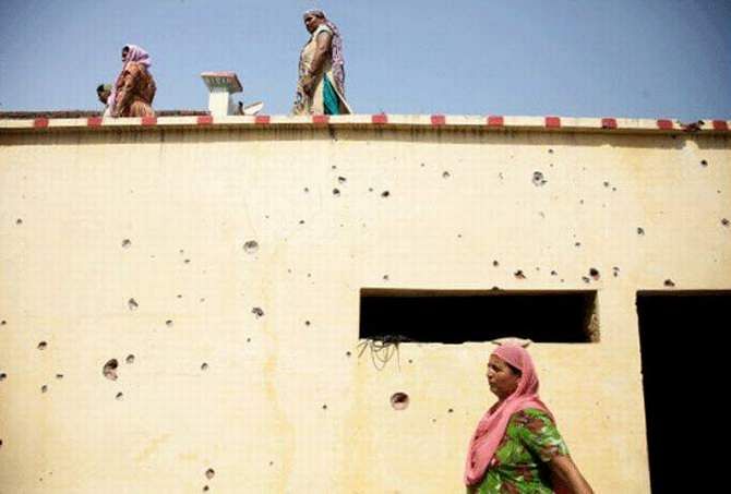 Women walk past a residential building with bullet marks allegedly fired from the Pakistan side at the India-Pakistan international border area of RS Pura on August 22, 2014. Photo: AP