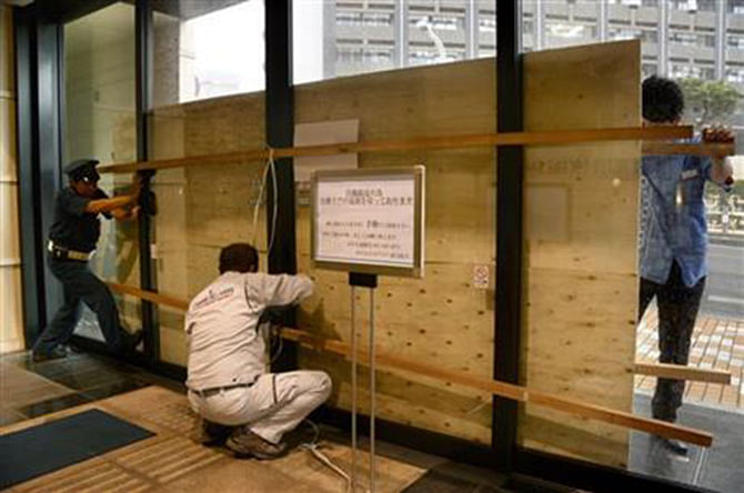 Hotel employees and a guard secure its entrance door with a plywood board in preparation for approaching typhoon Vongfong in Naha, Okinawa, October 11, 2014. Photo: AP