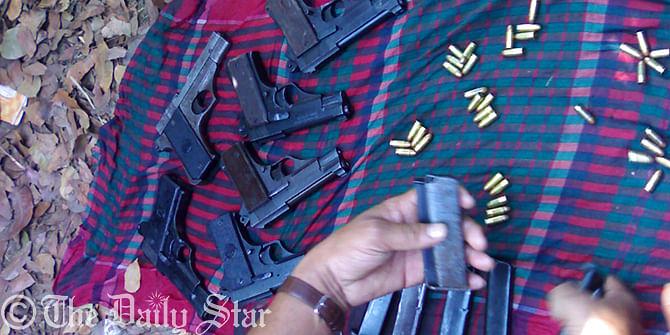 A policeman at Ghatail upazila of Tangail this morning inspects the recovered firearms, bullets suspected to be dumped by fleeing JMB militants snatched from police custody in Mymensingh Sunday. Photo: Star