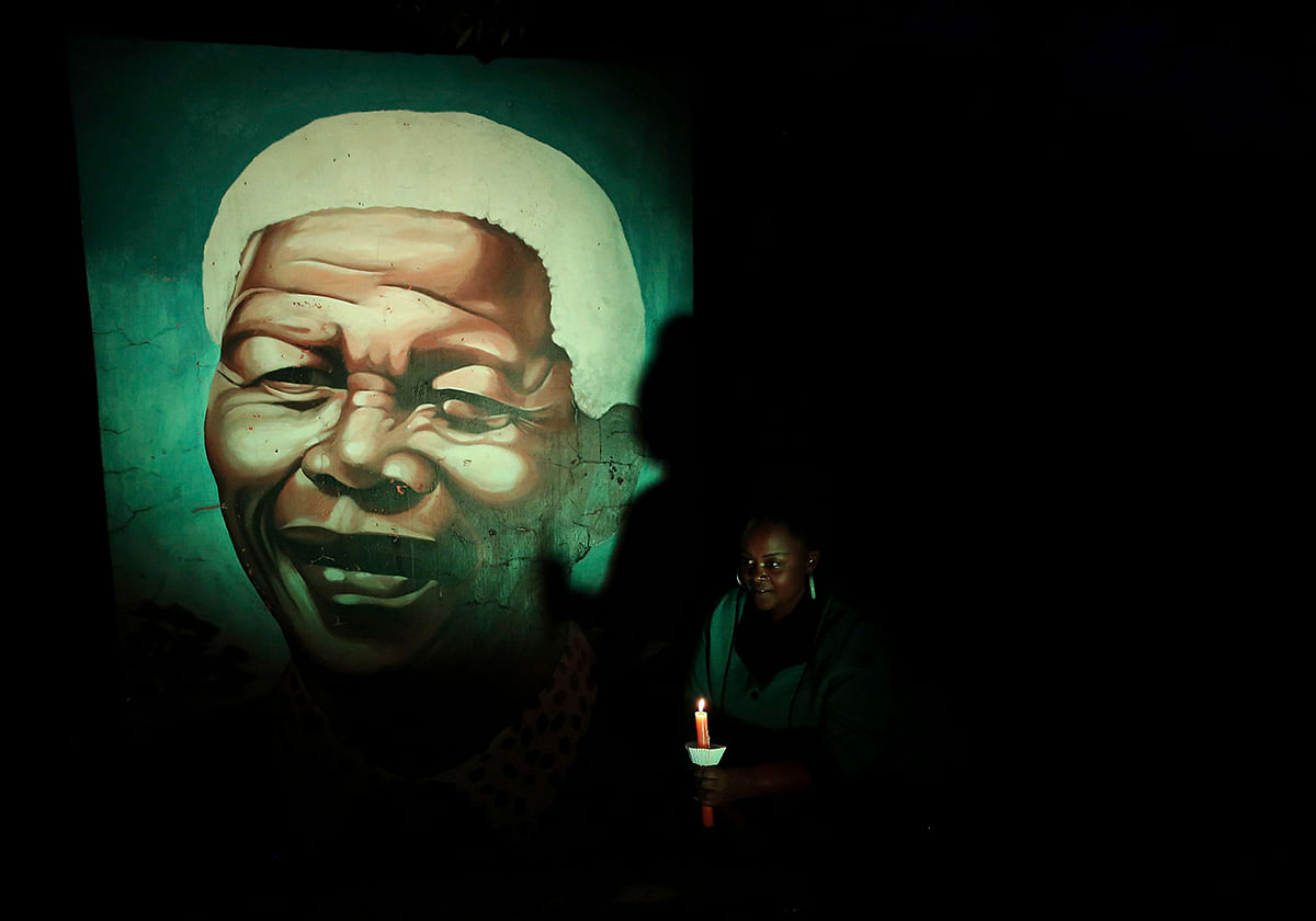 A local holds a lit candle in front of a mural of former South African President Nelson Mandela ahead of Mandela's first death anniversary, in Soweto December 4, 2014. Photo: Reuters