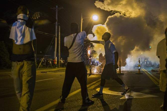 Protesters involved with a more vocal and confrontational group of demonstrators stand and gesture as tear gas is fired, at further protests in reaction to the shooting of Michael Brown near Ferguson, Missouri August 18, 2014. Photo: Reuters