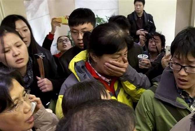 A woman, center, surrounded by media, covers her mouth on her arrival at a hotel which is prepared for relatives or friends of passengers aboard a missing airplane, in Beijing, China Saturday, March 8. Photo: AP 