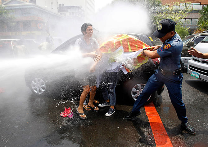 An anti-riot policeman grabs a banner from protesters as they are hit with a water cannon during a protest against the upcoming visit of US President Barack Obama next week, in front of the US embassy in Manila on Wednesday. Photo: Reuters