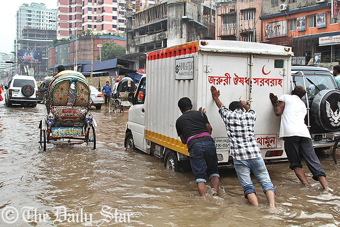 People are pushing a covered van that broke down as heavy rainfall flooded the road at Shantinagar in the capital on Monday. Inadequate rain water drainage system puts city dwellers in misery during the monsoon. Photo: Firoz Ahmed
