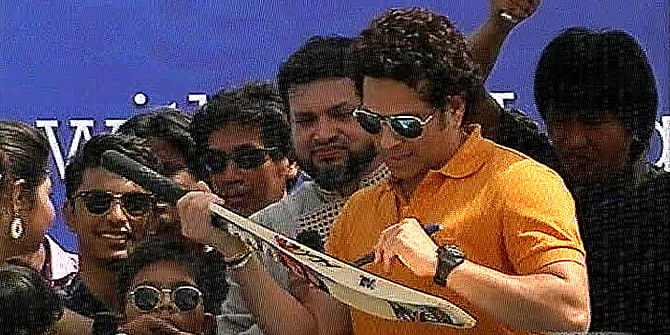 Star cricketer Sachin Tendulkar gives autograph on a bat on request of a fan at a primary school in Rupganj of Narayanganj on Tuesday. Photo: TV grab