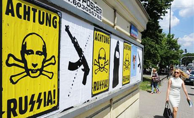 In the July 14 photo a woman passes by posters that express Polish opposition to Russia, in Warsaw, Poland. The posters imply a comparison of Russia today with Adolf Hitler’s Germany. Photo: AP