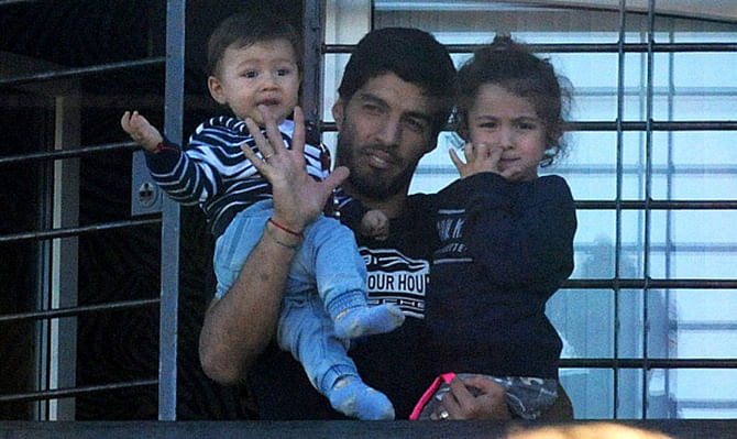 Uruguay's striker Luis Suarez, banned from football for four months after biting an opponent at the World Cup, holds his children as he greets fans from his mother's home in Lagomar, in the department of Canelones, near Montevideo, on June 27, 2014. Photo: Getty Images 