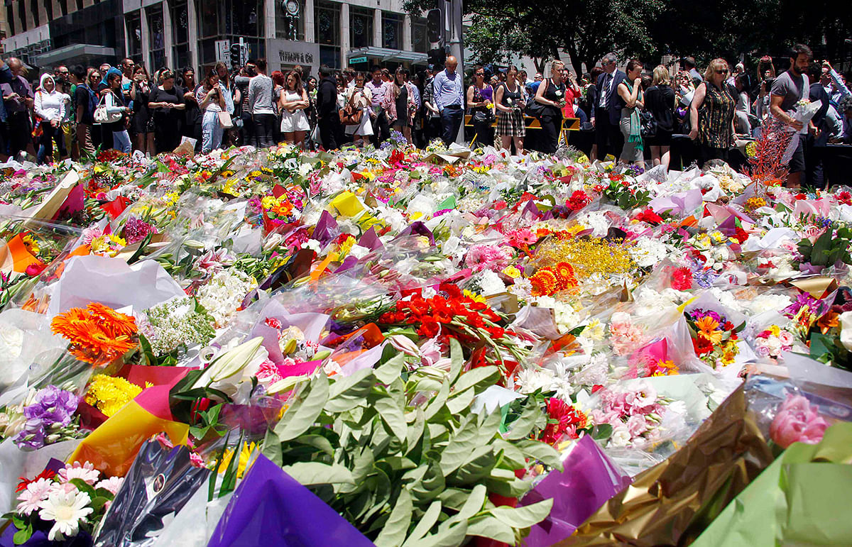 Members of the public look at floral tributes placed near the cafe where hostages were held for over 16-hours, in central Sydney December 16, 2014. Heavily armed Australian police stormed a Sydney cafe early on Tuesday morning and freed terrified hostages held there at gunpoint, in a dramatic end to a 16-hour siege in which two captives and the attacker were killed. Photo: Reuters