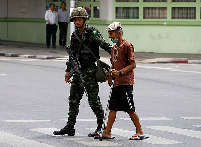 A Thai soldier helps an aged man cross a road outside the Army Club in Bangkok on Tuesday. Photo: Reuters