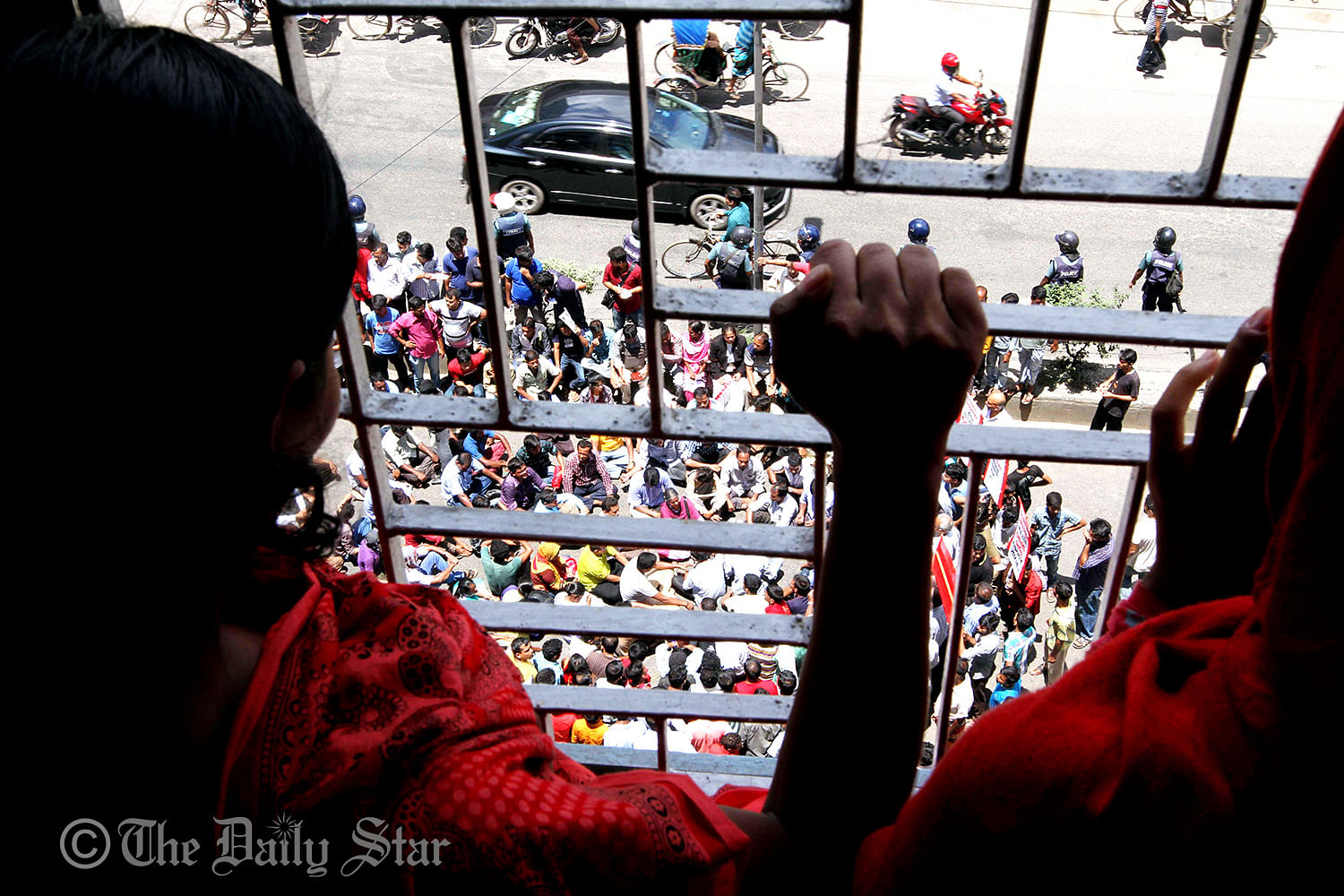 Two female workers of Tuba Group, who are observing hunger strike inside the factory demanding their due salaries, watching the sit-in programme organised by their colleagues and activists of left parties Friday in front of the factory on Gulshan-Badda link road in the capital. Photo: Palash Khan