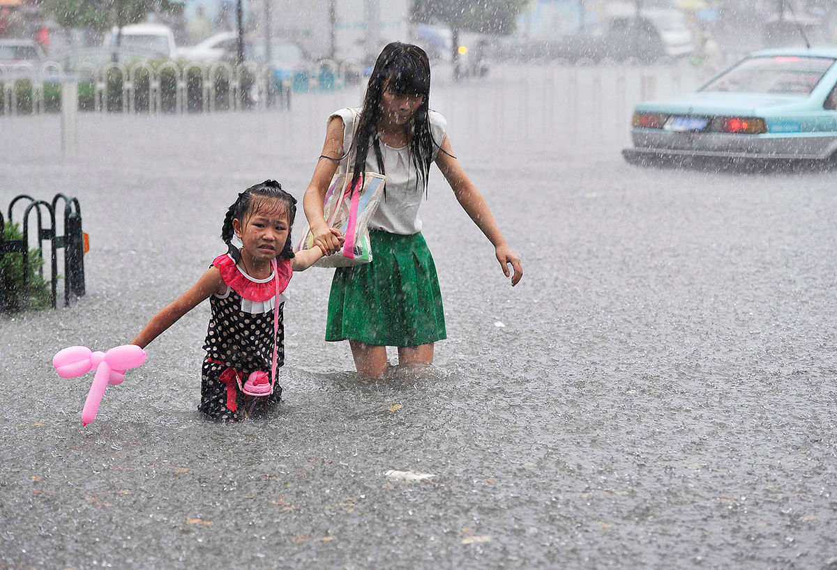 A mother holds her daughter as they wade across a flooded street during heavy rain in Hefei, Anhui province, July 27, 2014. Photo: Reuters