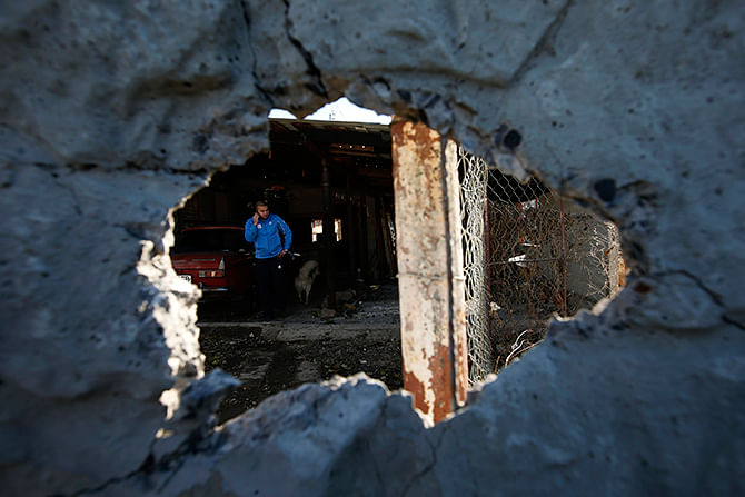 A man talking on a phone in his home, is seen through a hole in a wall damaged by recent shelling in Donetsk, eastern Ukraine, November 6, 2014. Photo: Reuters