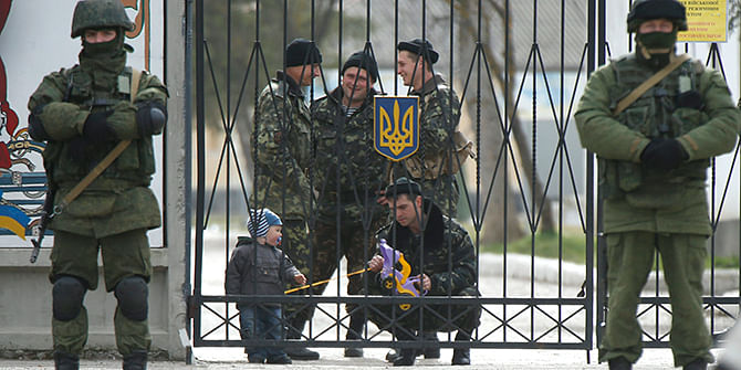 A Ukrainian serviceman plays with a child as men believed to be Russian servicemen stand in front of the gates of a Ukrainian military unit in the village of Perevalnoye outside Simferopol on March 4. Photo: Reuters